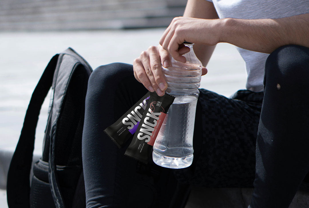 Person holding a water bottle and a SNCK bar outdoors